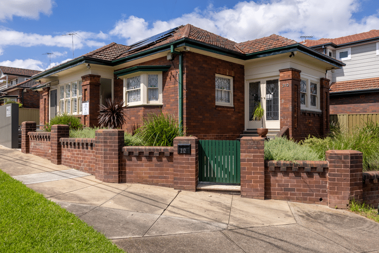 Five Dock Osteopathic and Chiropractic red brick house with a heritage colour scheme of green and cream. The house has an Australian native garden and red brick fence. Solar panels can be seen on the roof. The house has leadlight windows and doors