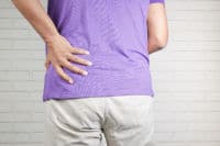 young man in blue shirt suffering back pain on the left side of back at pelvis height. The man is facing away from the camera