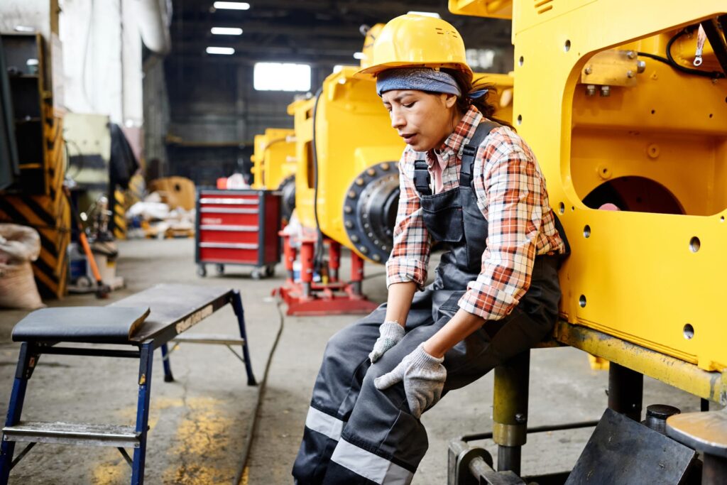 Trade worker wearing high vis clothing. and a yellow hard hat. The female worker is sitting clutching her left knee. She has a knee injury from work. Knee injury May require surgery. Knee pain treatment.