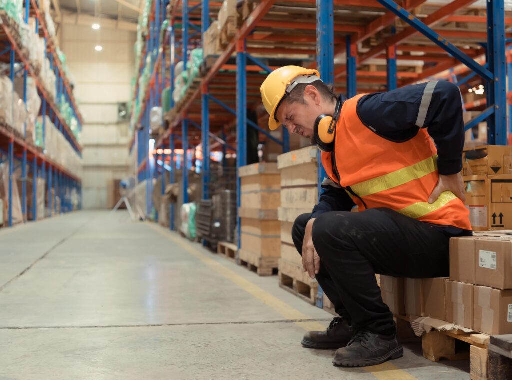 Warehouse worker sitting holding his back in hi vis dress. He has an anguished look on his face