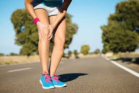 runner standing on the road bent forward holding their knee. wearing blue and pink shoes. Knee pain treatment for athletic performance.