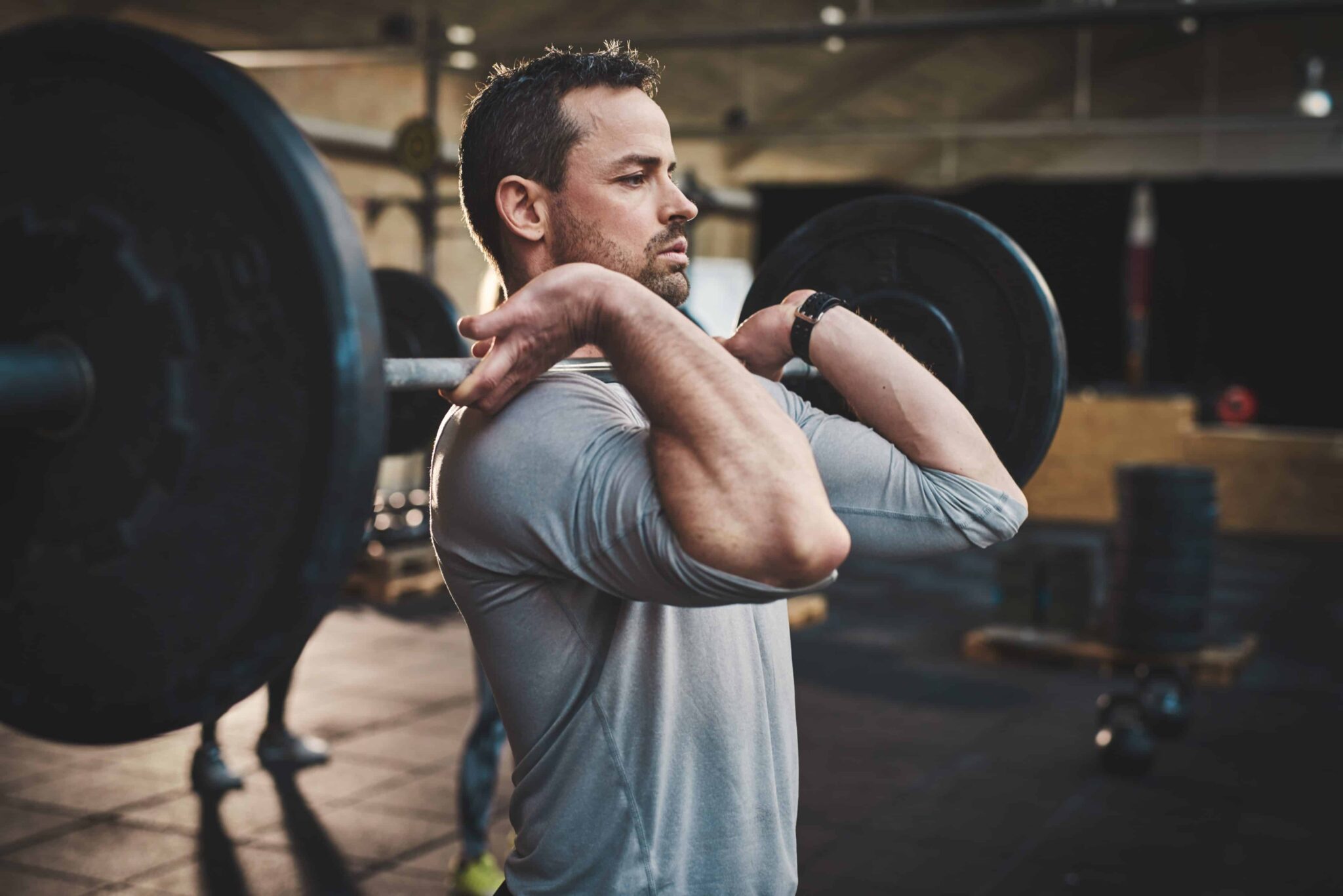 male in grey shirt performing a front barbell squat in a gym.