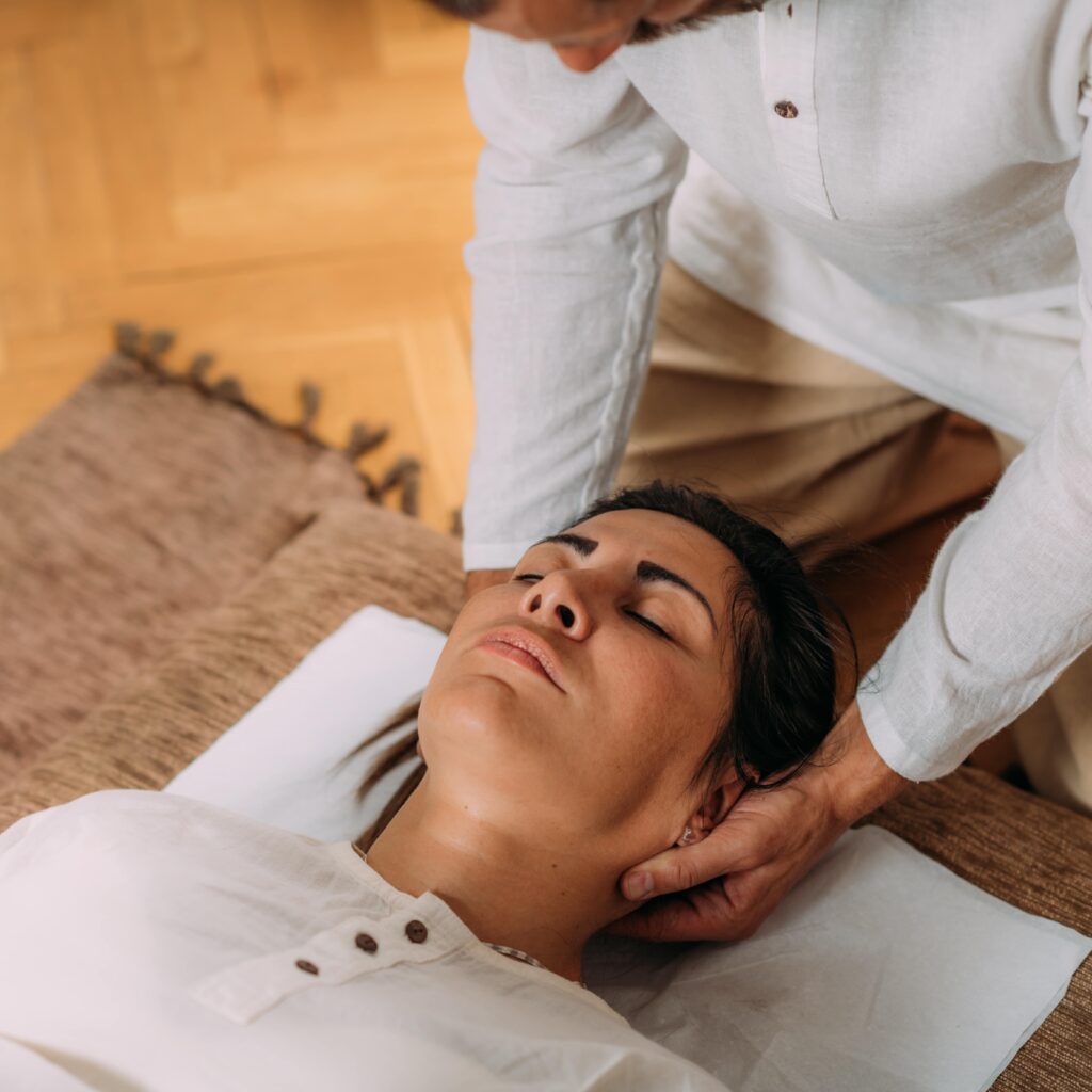 Remedial massage. a young lady getting massage on her neck. She is wearing a white top. The setting is a timber floor and brown table to lye on.