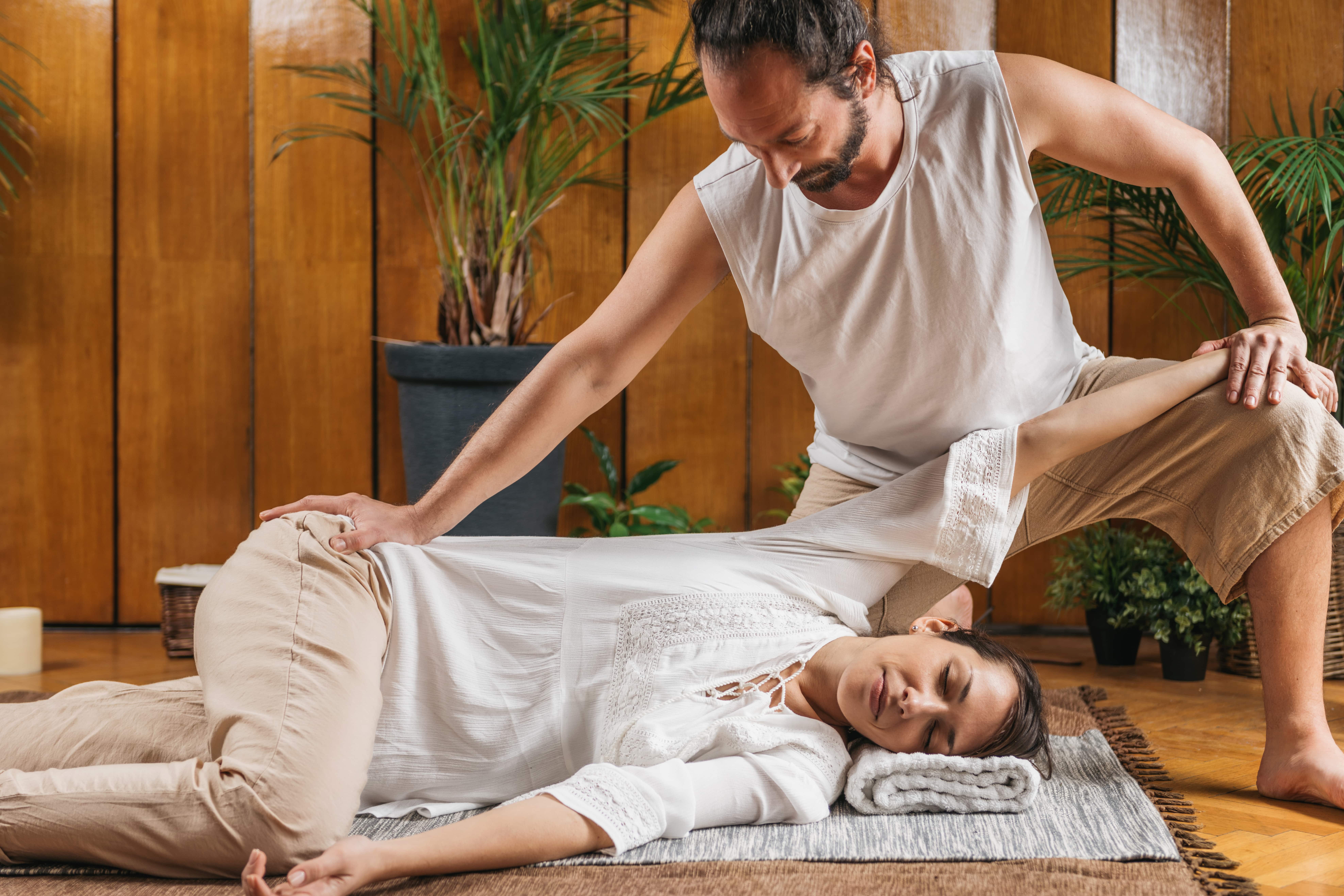 Man performing stretch with massage on young lady. The massage therapist is wearing white