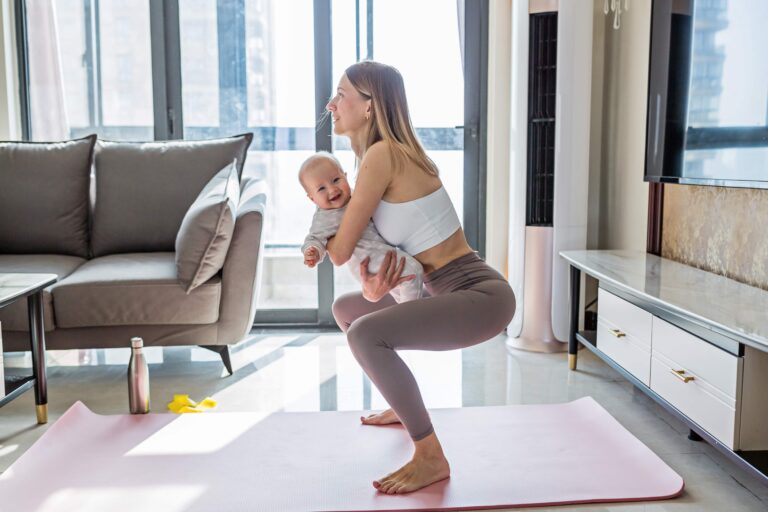 A lady carrying a baby doing exercise. She is wearing active wear. She has no pain and is smiling