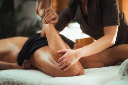 Remedial massage Burwood. Muscle pain from sports-related injuries, relief from massage. A young man having massage of his left leg to relieve muscle tightness.