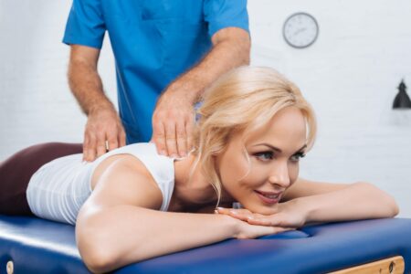 Lady lying face down on treatment table, with doctor palpating mid back. Chiropractic and Osteopath