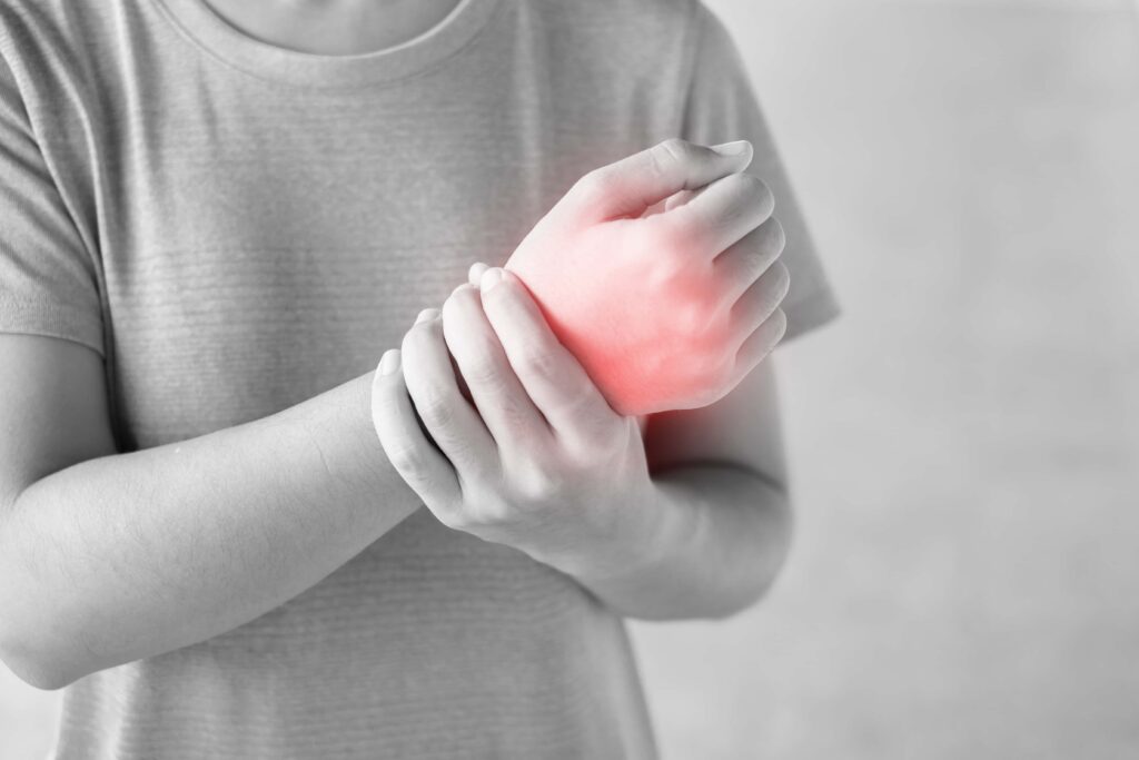 Lady wearing a grey shirt holding her wrist in pain. Wrist pain shown in red. Chiro wrist pain.