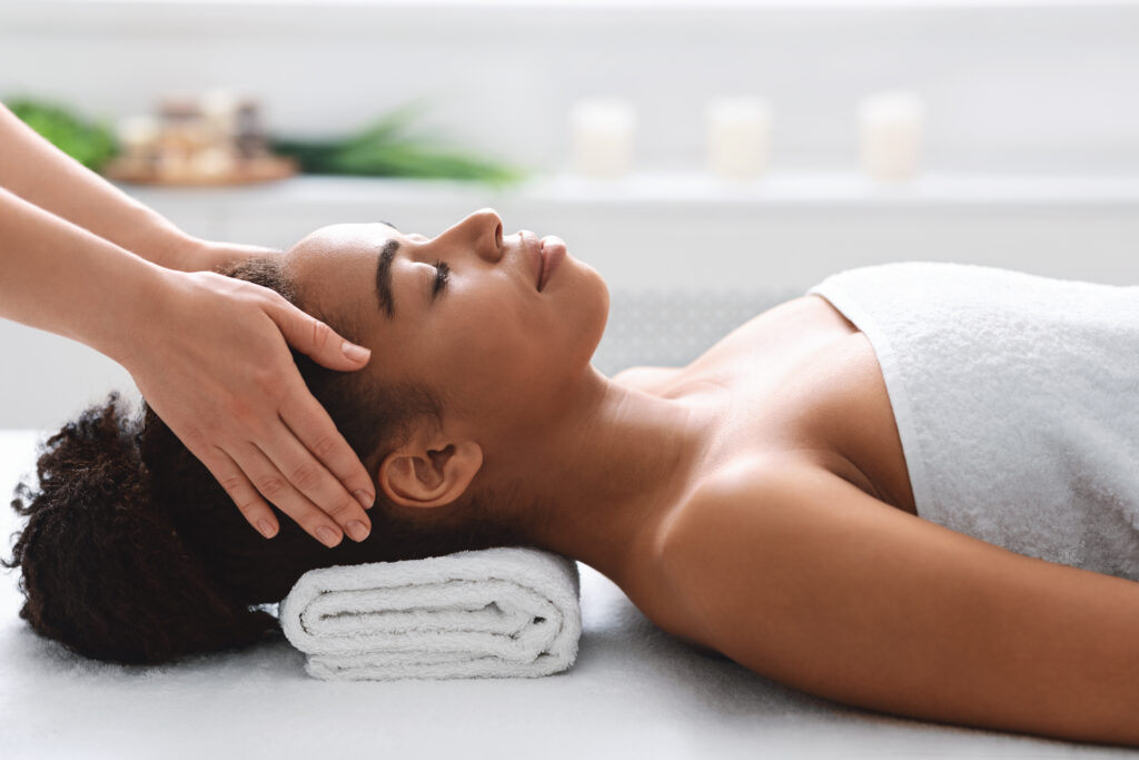 young african american woman getting head massage from massage therapist, side view