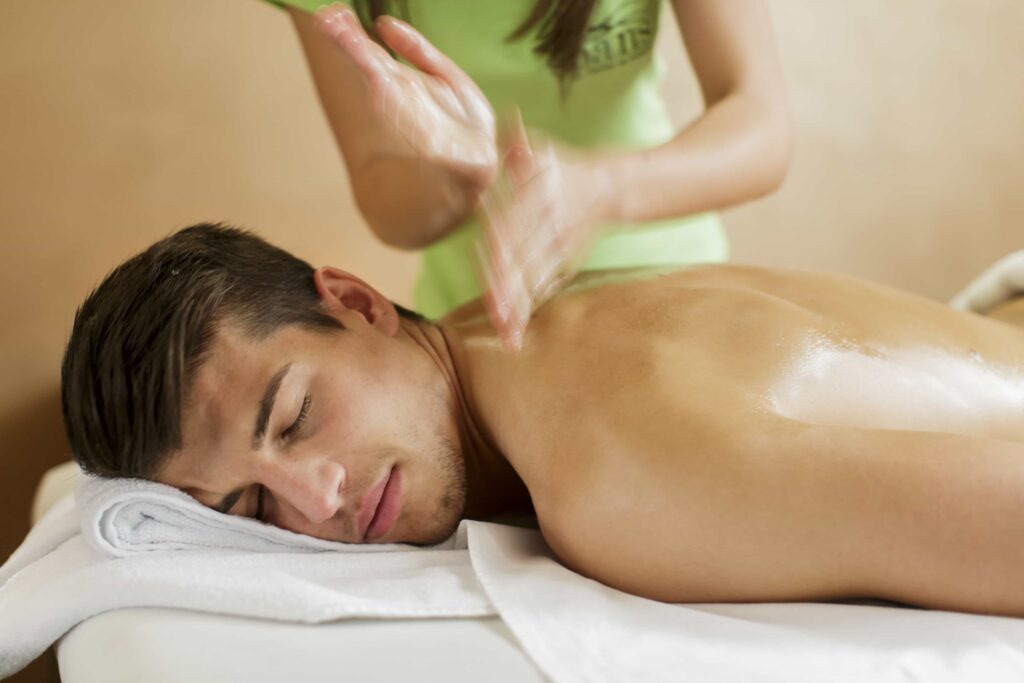 Sports massage, man lying on table having shoulders massaged. Oil massage. Massage therapist is wearing a green top. Sports Massage Five Dock
