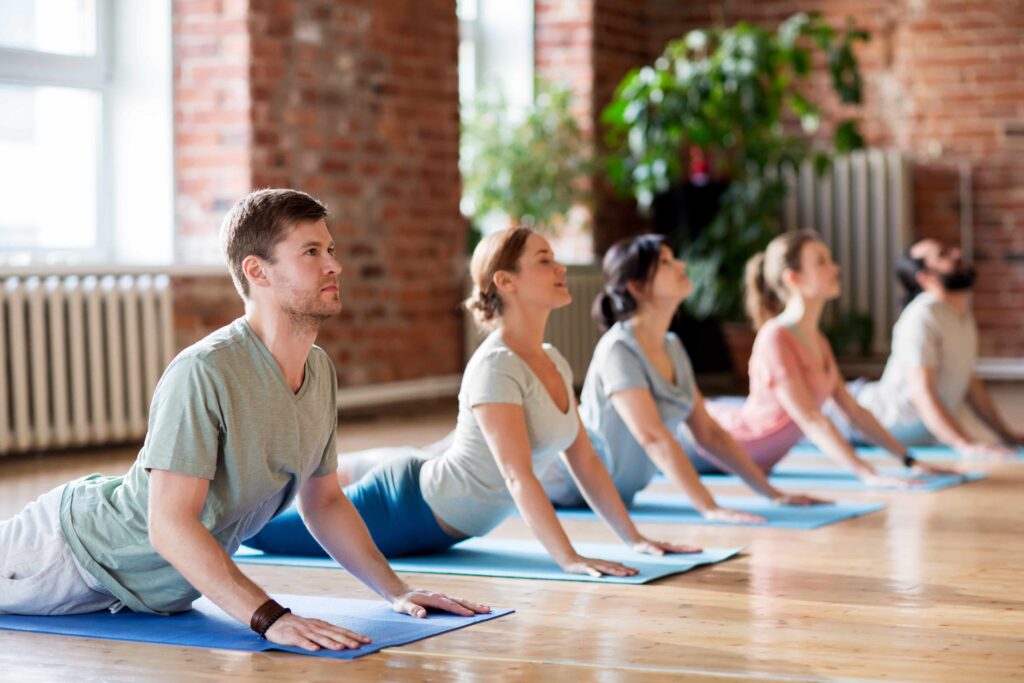 Group of five people doing yoga on, yoga mats. The class is a wooden floor with open windows behind the group. Picture is to show how gentle movement can calm the nervous sytem.