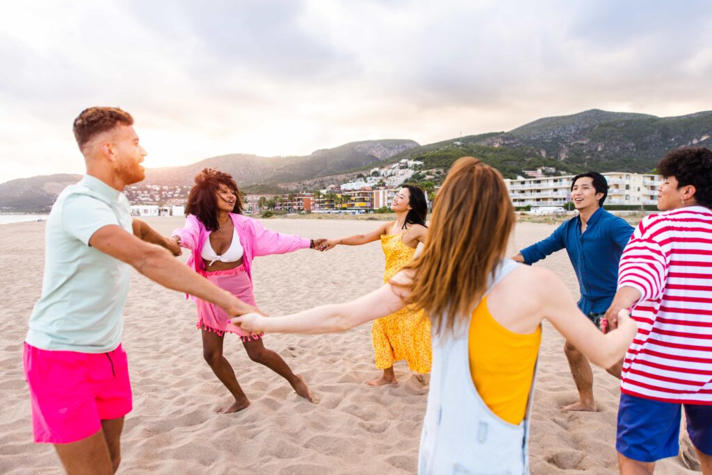 Walking in a circle on the beach, on a cloudy day. It is a young group of five people. They are wearing colourful clothes.