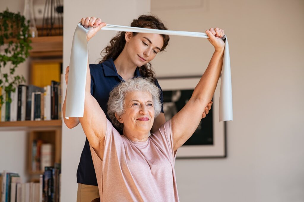 An elderly lady is using TheraBand to strength her shoulders. Prevention of shoulder pain and rotator cuff muscle tears.