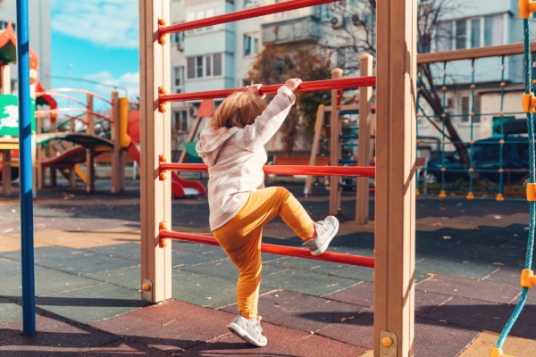 Picture of child from behind climbing up crossbars. Crossbars are orange with timber posts. Having good fascia elasticity allows for good reach.