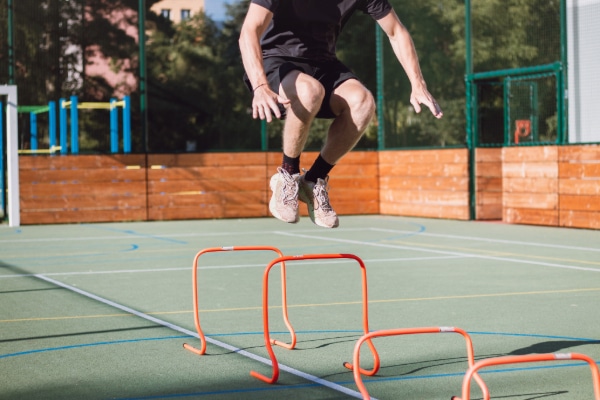 Male track athlete jumping over orange hurdles