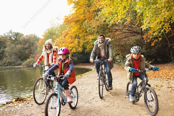 Health span family riding bikes. Four members of the family riding along a lake in the autumn.