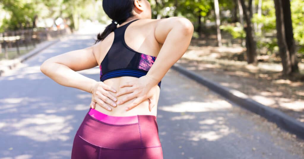 young lady running down a garden path in active wear has stop an is clutching lower back. Lower back arthritis can cause this reaction to the pain.