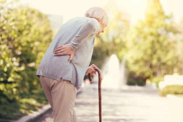 woman holding a walking stick and walking while feeling pain in the back. She can be suffering from hip spine syndrome.