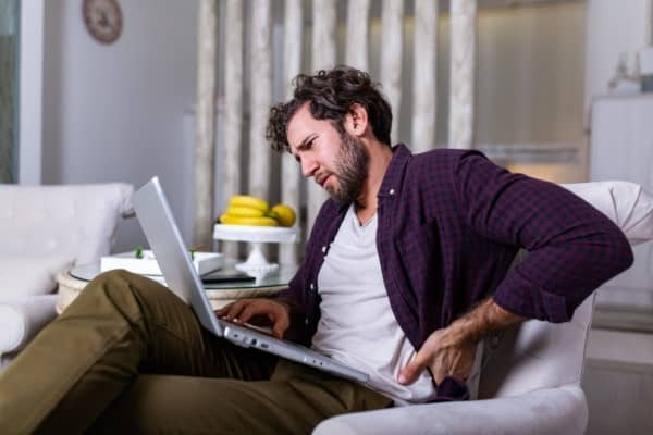 Lower back pain on left side of man sitting on lounge with computer. Haberfield chiro service to fix pain picture.