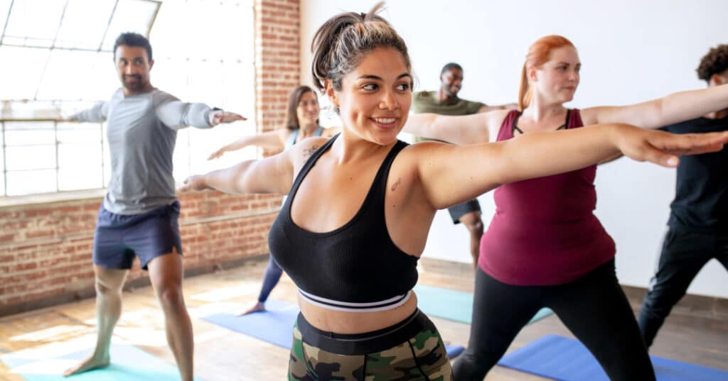 Group doing a yoga class. Warrior pose to stretch lower back and legs. Arms abducted to work shoulders