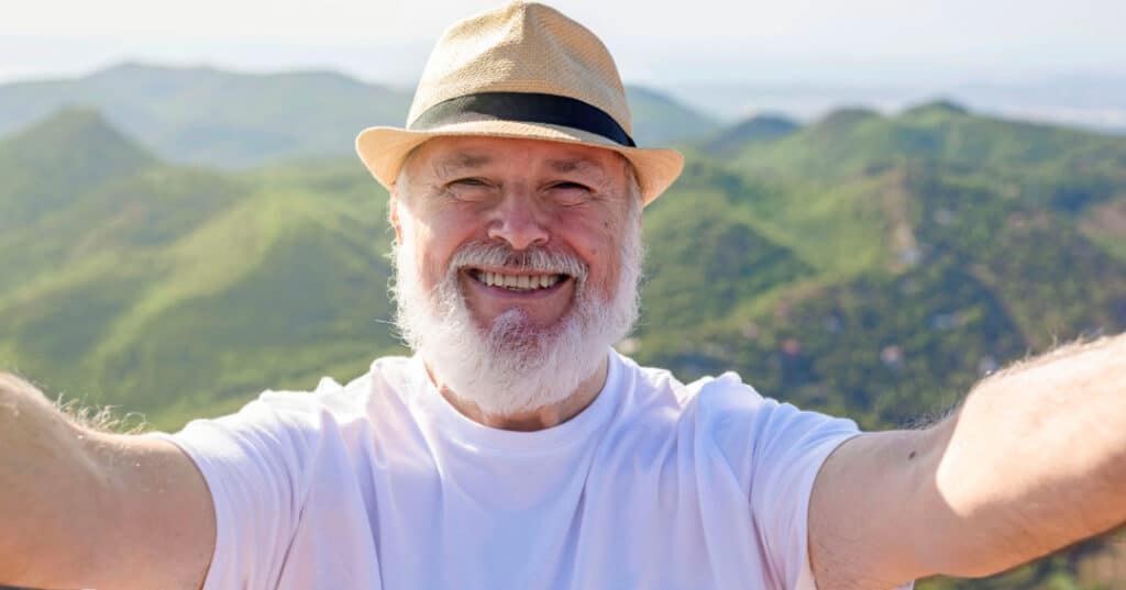 Smiling gentlemen with mountains in the background. He is wearing a straw hat.