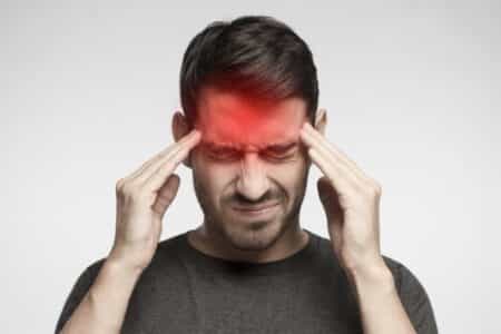 Portrait of young man isolated on gray background, suffering from severe headache, pressing fingers to temples with closed eyes. Headache from stress.