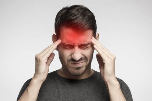 Portrait of young man isolated on gray background, suffering from severe headache, pressing fingers to temples with closed eyes