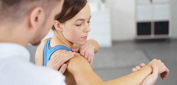 Lady having her right shoulder treated by a chiro. she is sitting with her arm raised. the male chiro is supported the arm and palpating her shoulder. Osteopath shoulder treatment. bursitis or rotator cuff injury. She is wearing a blue singlet.