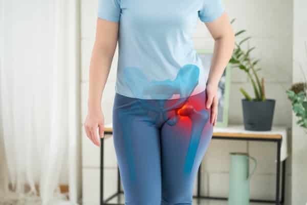 Hip joint pain, woman suffering from osteoarthritis at home, health problems concept. Lady is wearing all blue and standing holding left hip.