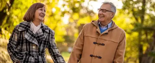 Couple walking through a park holding hands and smiling. Wellness care is represented by being older and happy because they have good health