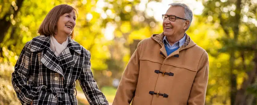 Couple walking through a park holding hands and smiling. Wellness care is represented by being older and happy because they have good health