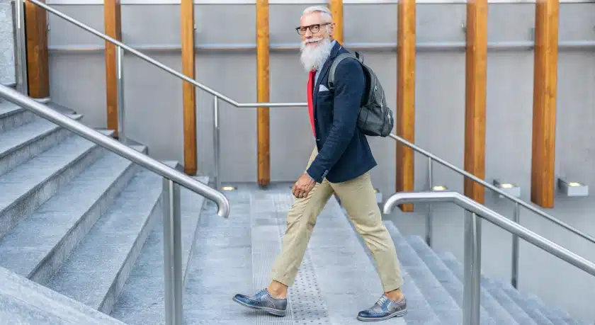 Man with a grey beard wearing a blue suit is walking up stairs. Movement promotes a health life span and physical, emotional and mental wellbeing.