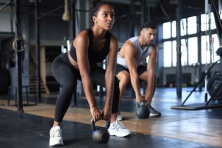 Fit and muscular couple focused on lifting a dumbbell during an exercise class in a gym. Strength and stability training. Functional movement exercises being performed.