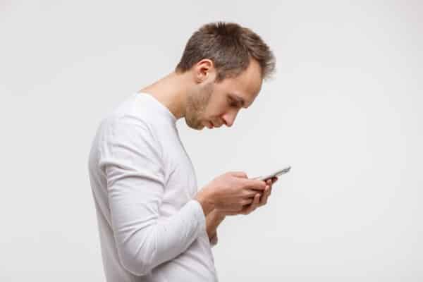 Close up portrait of man looking and using smart phone with scoliosis, side view, isolated on gray background. Rachiocampsis, kyphosis curvature of neck, Incorrect posture, leading to tech neck.