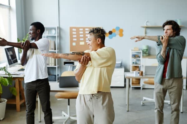 Diverse group of smiling young people doing stretching exercise during warm up break in office