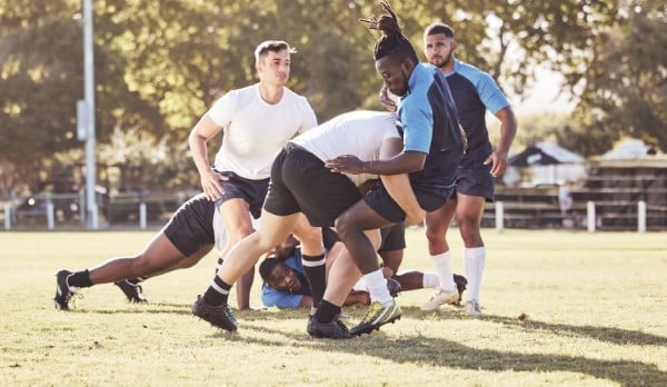 Rib pain from injury caused by contact sport - rugby. Two teams playing rugby in a park