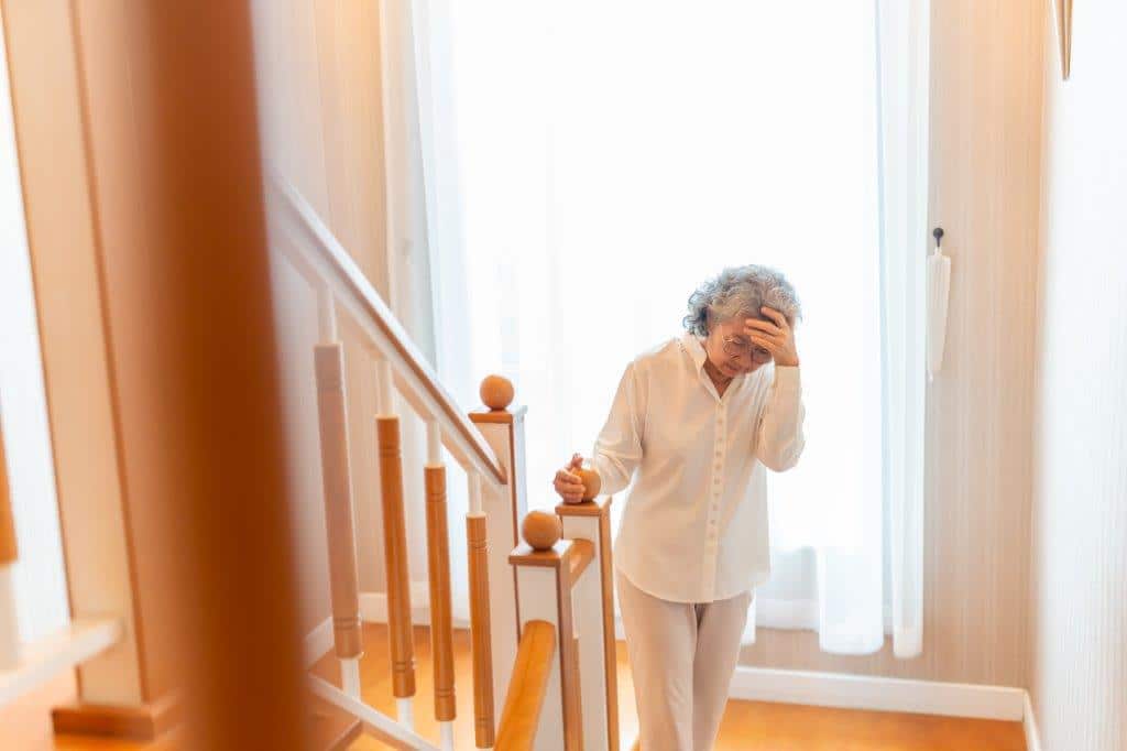 Fibromyalgia patient in pain, standing at the bottom of a set of stairs. Patient looks in physcial discomfort and is holding head from the pain.