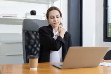 Young lady sitting at a computer with a muscle strain in her neck from bad posture