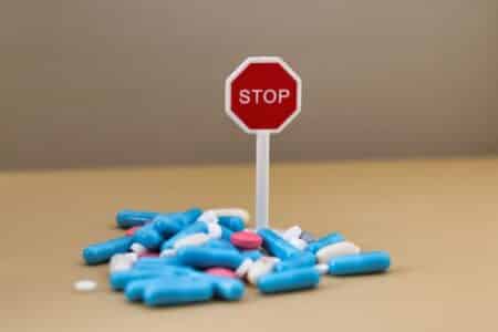Drug addiction; stop taking so many medications; stack of multi-colored pills with a stop sign
