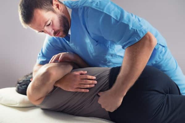 male Chiropractor in blue shirt performing a chiropractic Back Adjustment