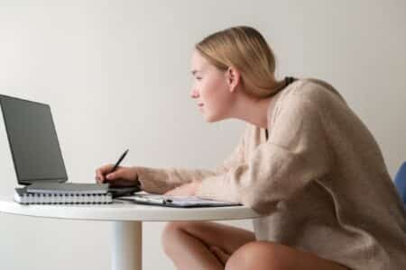 young woman sitting with poor posture shoulders slumped and hunched over a desk working on her laptop