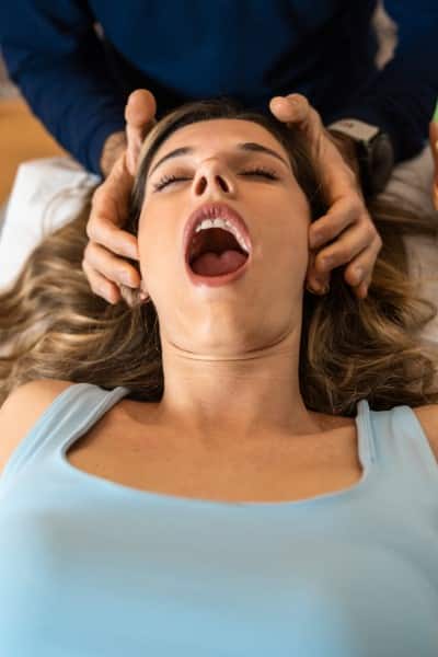 A young female patient is having muscle work performed by an osteopath on her jaw. She is lying on her back.