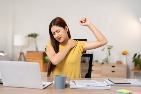 Asian businesswoman with shoulder pain from sitting at work all day. Massage for overworked shoulders. Health and office syndrome concept.