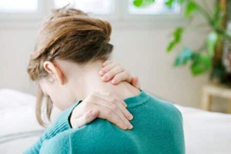 Lady siting on table holding her neck in pain. She is seeing an osteopath who fixes neck pain.