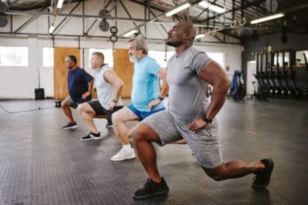 People, fitness and stretching legs in class with personal trainer at gym for workout, exercise or training. Diverse group in warm up leg lunge session with coach for cardio wellness on floor