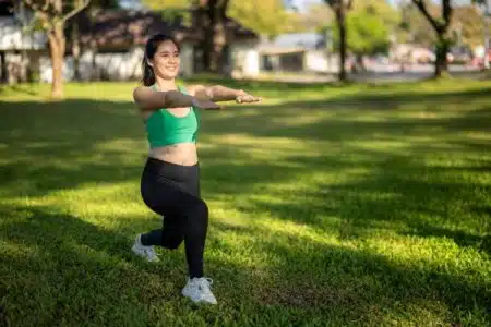 lady doing exercise in a park to relieve stress. She is wearing a green top and black pants.