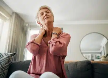 Low mood shown as lady sitting on lounge holding her neck looking depressed.