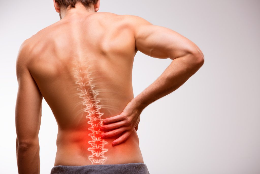 Lower back pain from sitting shown as man standing holding his back, with red light coming from his lumbar spine.