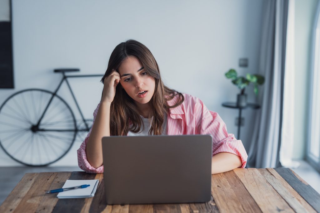 Headache shown as lady sitting at a desk working her computer, holding the side of her head.