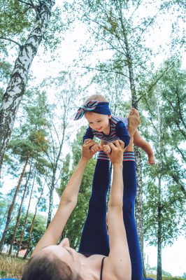 Mum and baby out in a forest setting. The mum is stretching and playing with the bab on her feet. The mum is on her back.